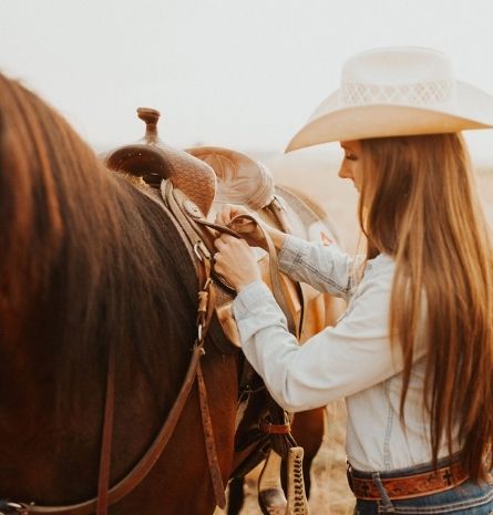 Woman wearing a cowboy hat saddling a horse